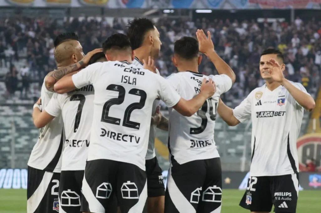 Jugadores de Colo-Colo celebrando un gol contra Unión Española con hinchas de Colo-Colo en el Estadio Monumental de fondo.