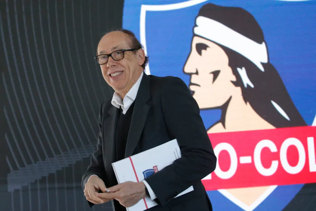 Alfredo Stöhwing sostiene una carpeta en sus manos y de fondo está el logo de Colo-Colo en una pantalla.