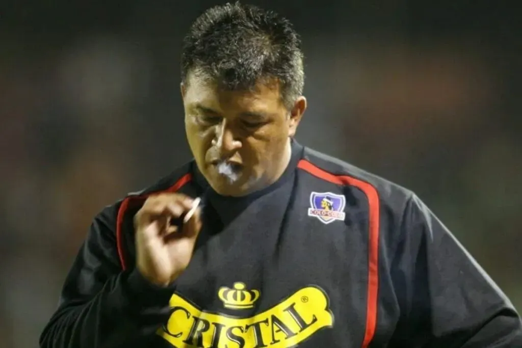 Claudio Borghi con indumentaria de Colo-Colo mientras fuma durante un partido.