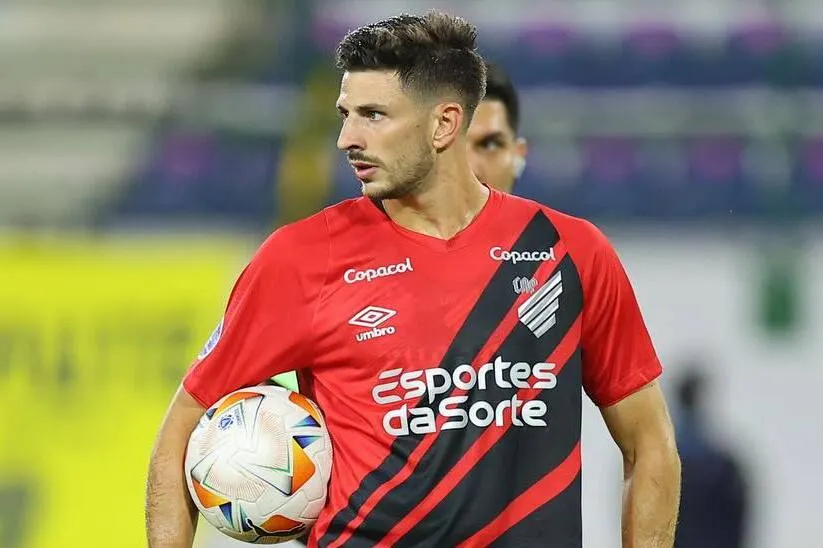 Primer plano de Lucas Di Yorio con la camiseta de Athletico Paranaense y un balón bajo su brazo.