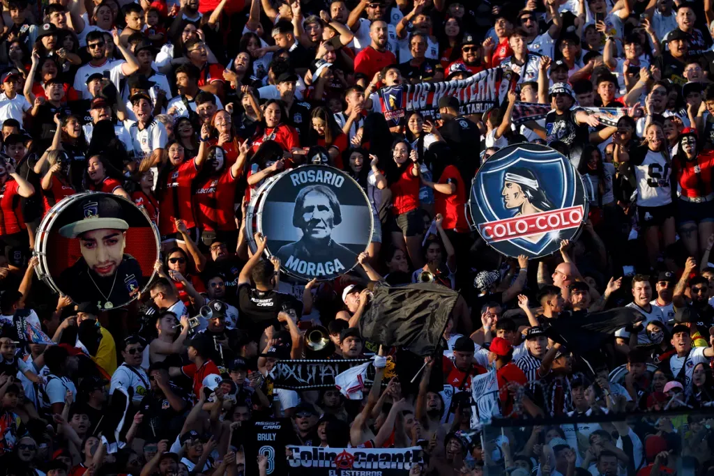 Hinchas de Colo-Colo alientan al equipo y levan tres bombos que representan a la institución durante la temporada 2024.