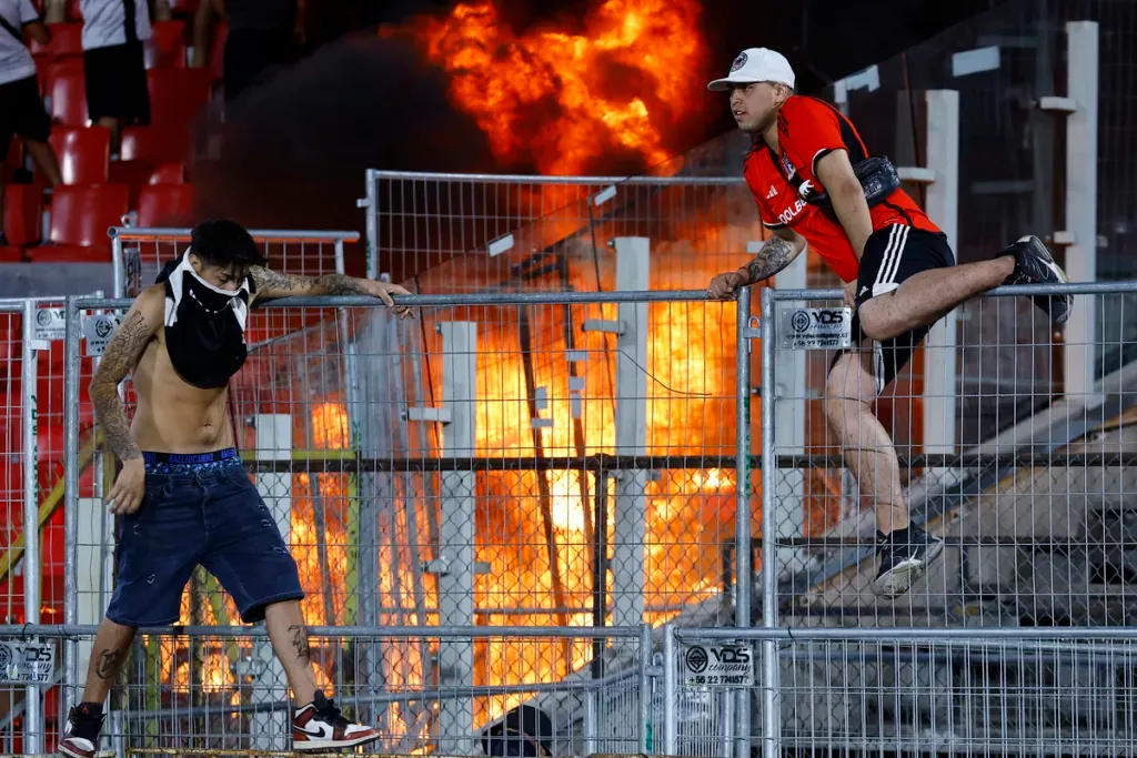 Hinchas de Colo-Colo sobre una reja mientras se quema la galería norte del Estadio Nacional.